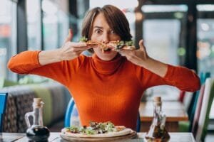 jeune-jolie-femme-mangeant-pizza-au-bar-pizza_1303-20333 Avoir une forte appétit qui peut mener à une addiction à la nourriture.