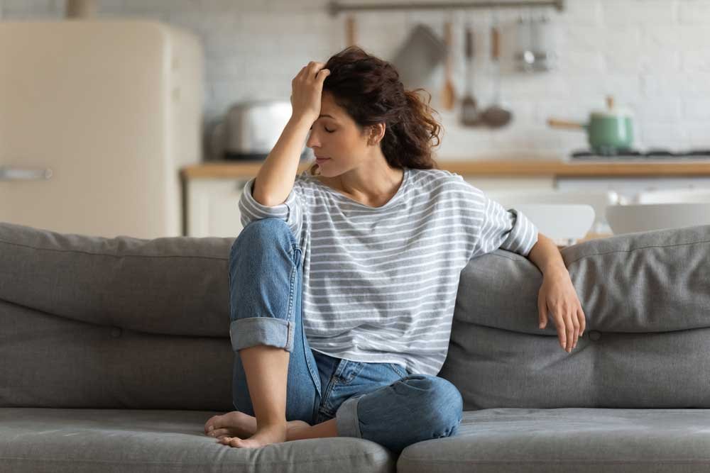 Une femme seule sur son canapé exprime sa dépression en se prenant la tête