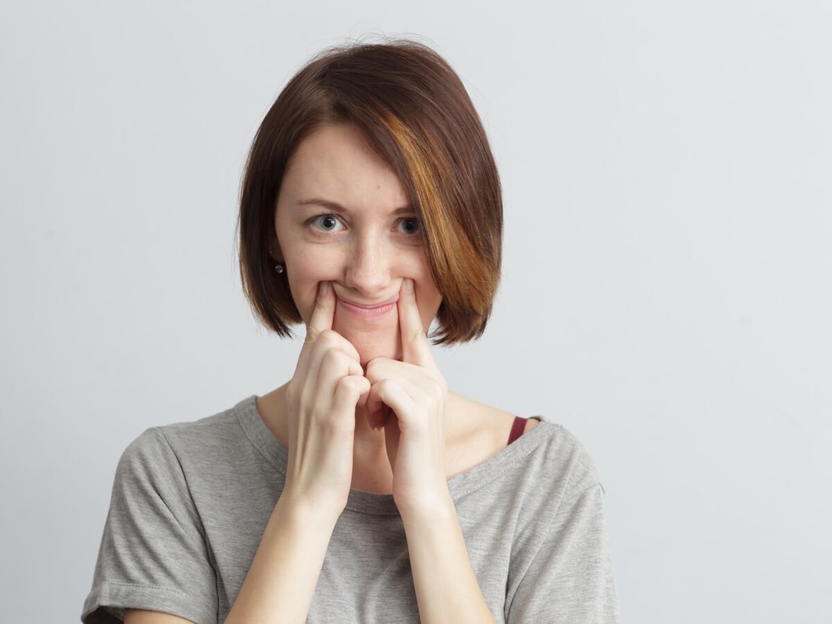 Une femme se force de sourire avec l'aide de ses mains, mais son visage exprime la dépression.