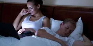 Une femme devant son ordi en pleine nuit, alors que son conjoint dors à côté.