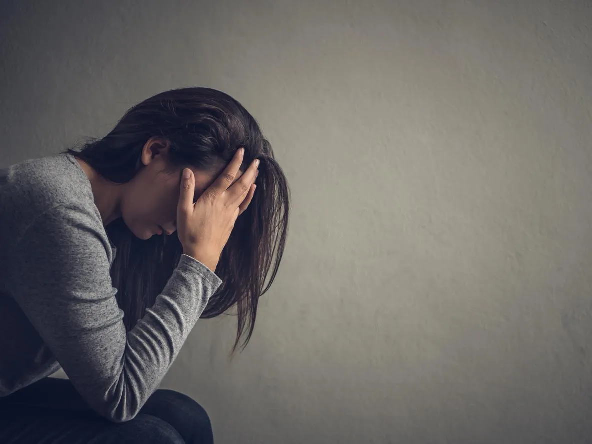 Une femme, la tête baissée, se couvrant le visage pour manifester sa dépression.