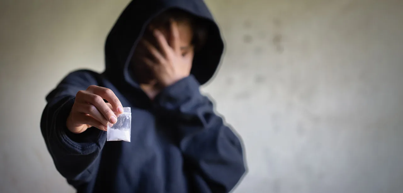 Une personne qui dissimule son visage, tenant un sachet de drogue.