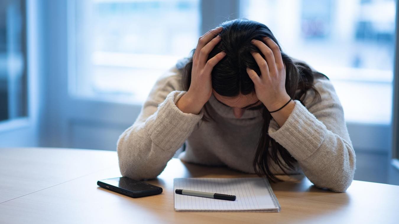 B9722967973Z.1_20200318110240_000+GS3FOACRJ.1-0 Une jeune femme penchée sur un bureau souffrante de dépression.