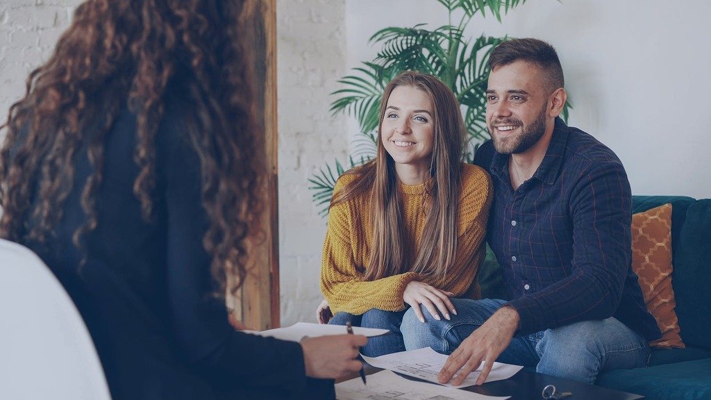 Couple discussing home options with agent in modern office setting.