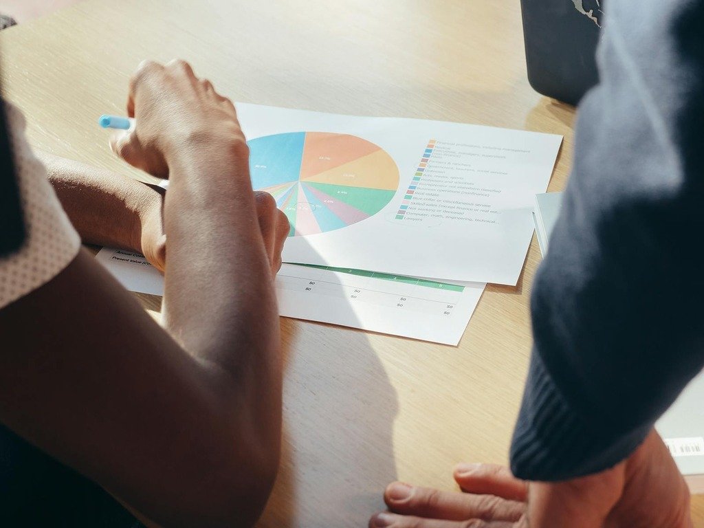 Two professionals collaborate on a project, examining a colorful pie chart in an office setting.
