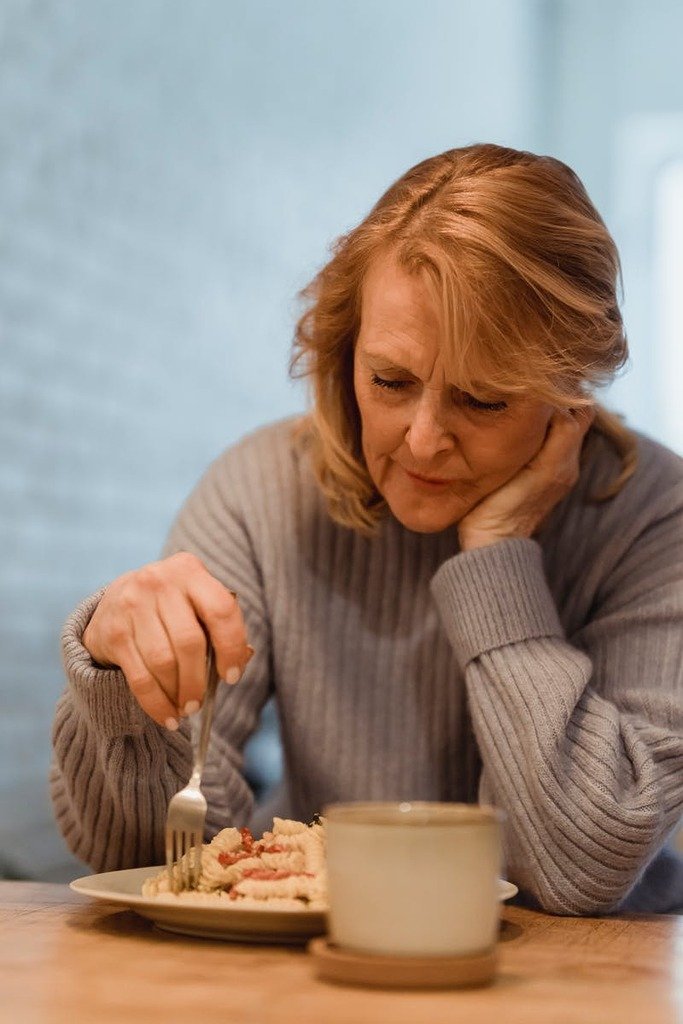 Senior woman in cozy sweater enjoying a hot breakfast with coffee indoors.
