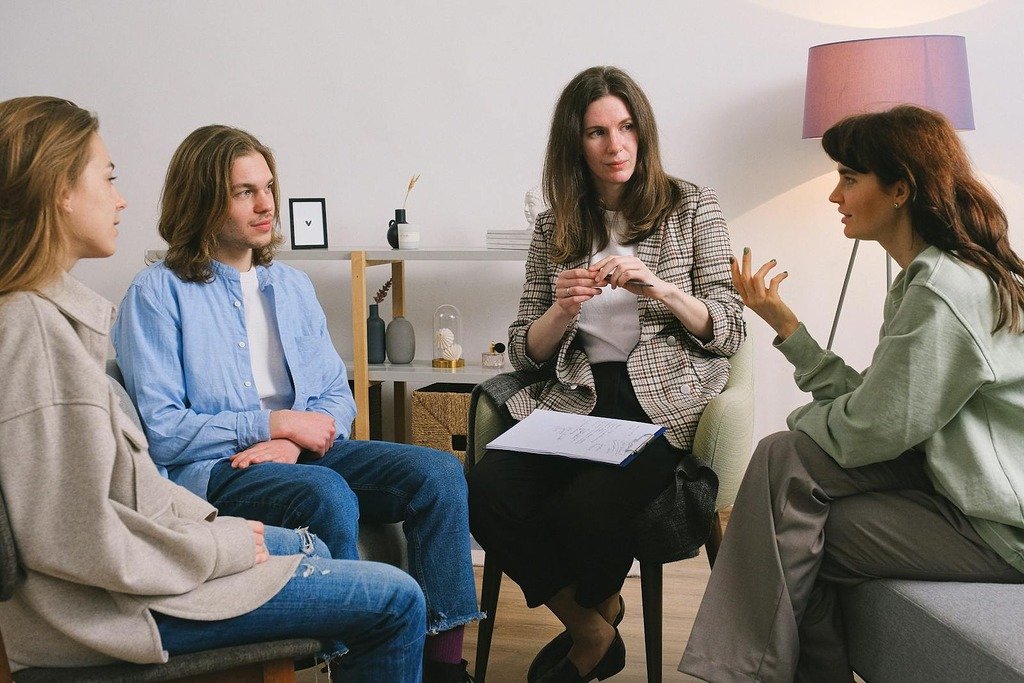 Female in casual clothes sitting on sofa and talking with psychologist and other people in group