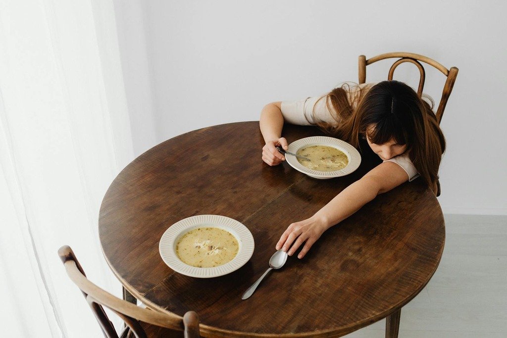 Woman lying down on a wooden table with two bowls of soup, creating a calm and serene scene.